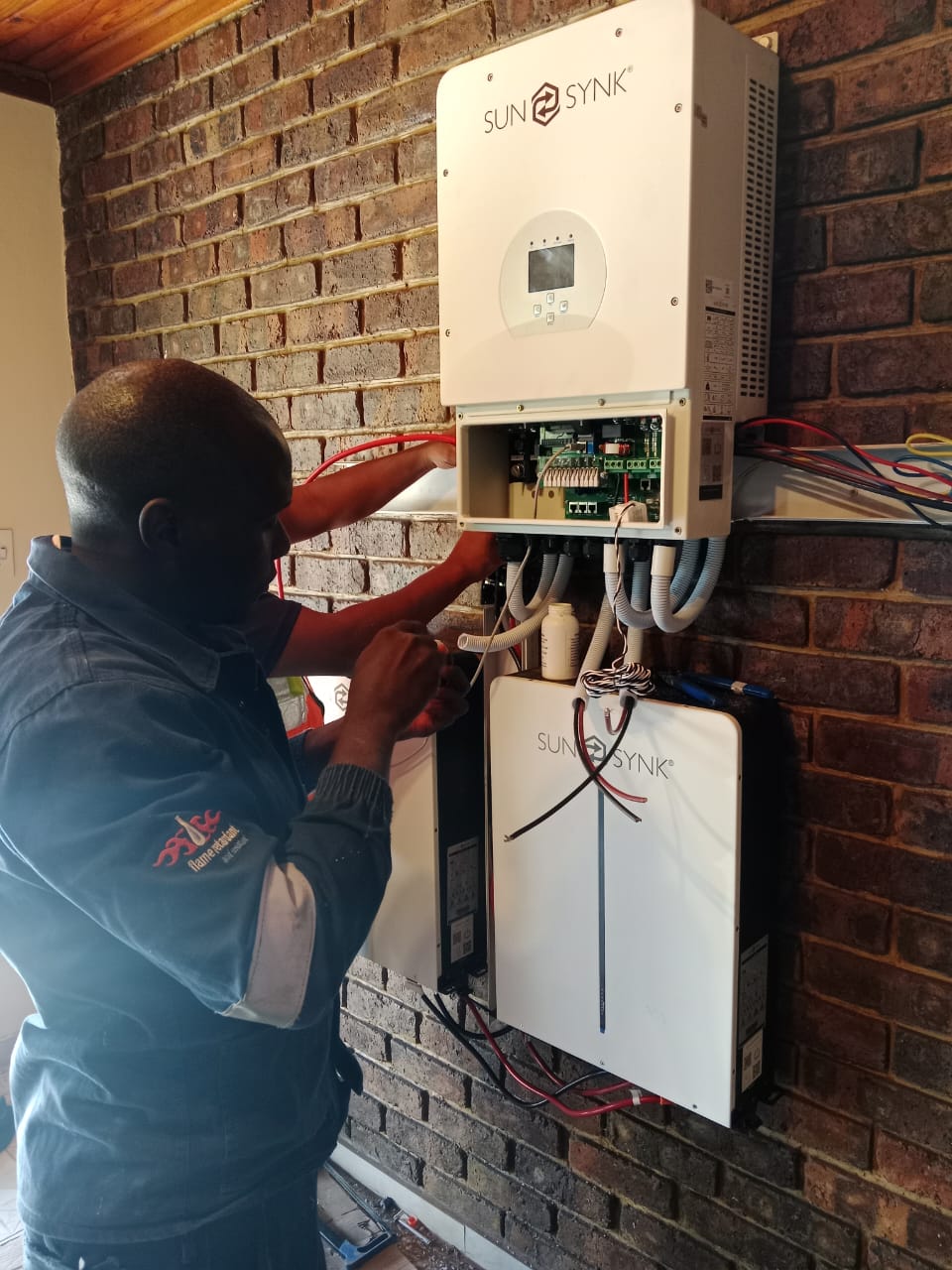 Technician connecting inverter and battery equipment on a brick wall
